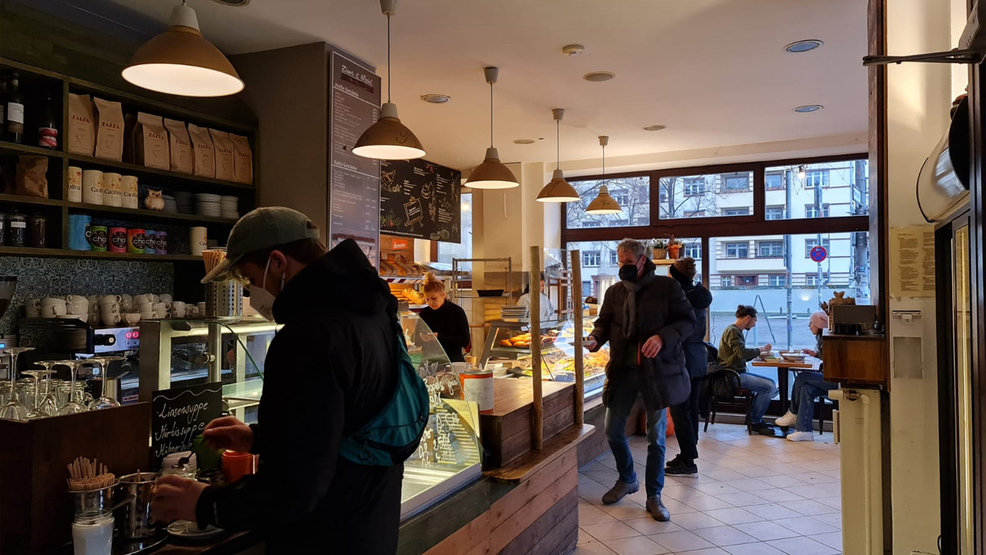 Der Innenraum mit Kaffeetheke, Pendelleuchten und Gästen
